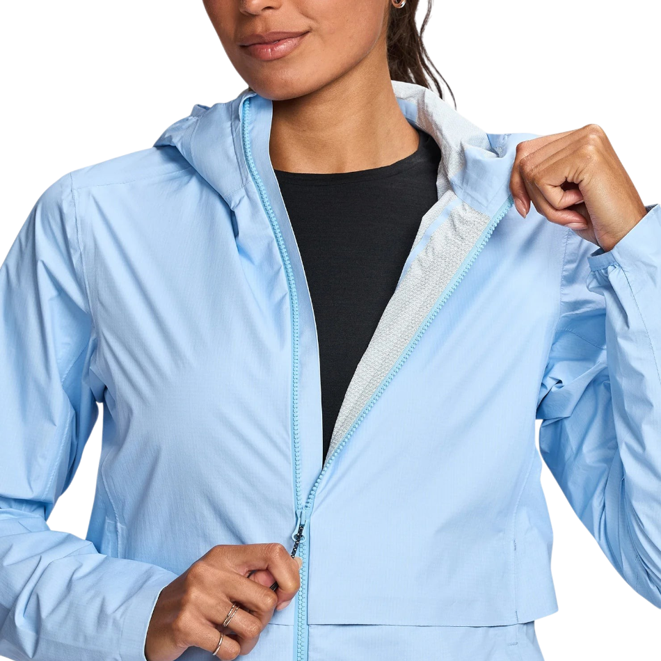 Up & Running Janji Women's Rainrunner Pack Jacket in light blue, featuring a hood and front zipper closure.